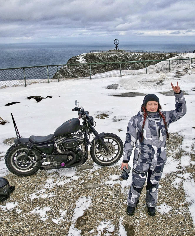 Bikerida poserar med sin hoj vid ett Nordkap i vinterskrud.
